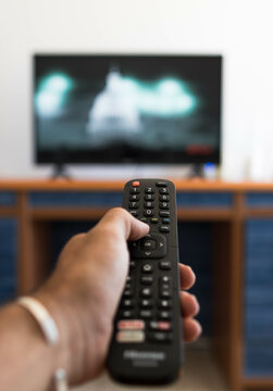 Vertical photo of a hand holding a television remote control while looking for a movie