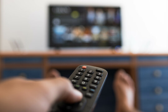 Hand holding remote control while searching for a series on television with hit feet on the table