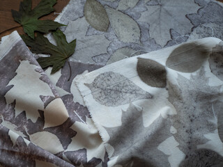 Fabric with leaves pattern and dried plants on the wooden table. Concept of eco print, botanical printing