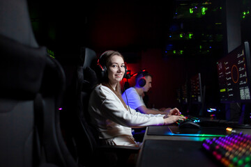girl gamer sits in headphones in a computer club looks at the camera and smiles, portrait of a...