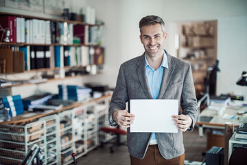 Middle aged man holding a blank paper in a startup company office with copy space