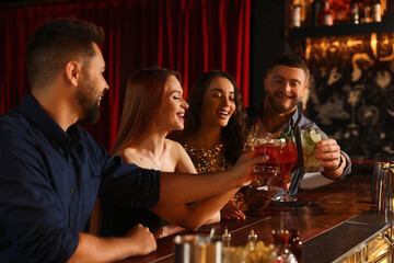 Happy friends clinking glasses with fresh cocktails at bar counter