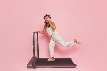 Student girl preparing for university, doing exercises on treadmill while curling hair and talking on phone, lifestyle concept, copy space