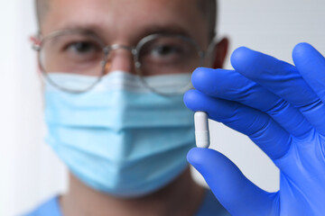 Doctor holding pill on light background, selective focus. Space for text