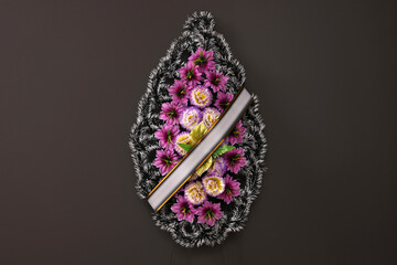 Funeral wreath of plastic flowers with ribbon hanging on dark grey wall