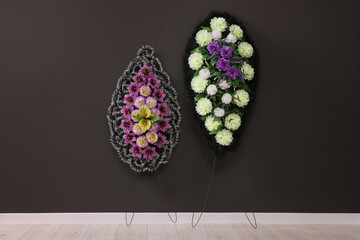 Funeral wreaths of plastic flowers hanging on dark grey wall indoors