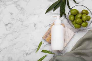 Obraz na płótnie Canvas Bottle of cosmetic product with olive essential oil and leaves on white marble table, flat lay. Space for text