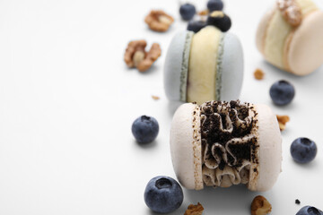 Fototapeta na wymiar Delicious macarons, walnuts and blueberries on white table, closeup. Space for text