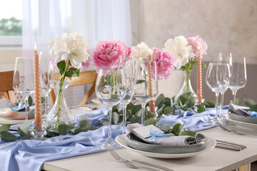 Beautiful table setting. Plate with greeting card, napkin and branch near glasses, peonies, burning candles and cutlery on table indoors