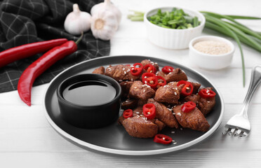 Plate with tasty soy sauce and roasted meat served on white wooden table