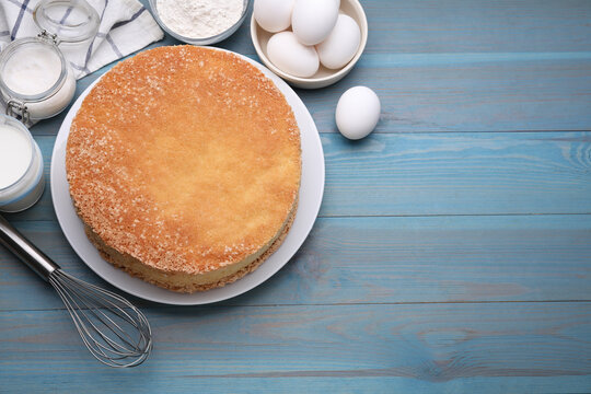 Plate with delicious sponge cake and ingredients on light blue wooden table, flat lay. Space for text