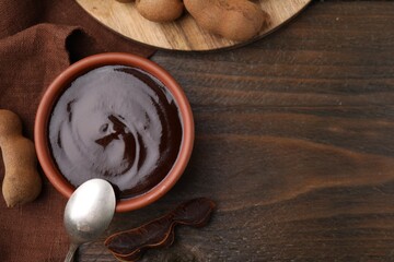 Bowl of tamarind sauce, spoon and fresh pods on wooden table, flat lay. Space for text