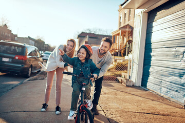 Young family walking and riding a bike on the sidewalk in the suburbs of the city