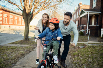 Young family walking and riding a bike on the sidewalk in the suburbs of the city