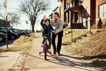 Father and son walking and riding a bike on the sidewalk in the city suburbs