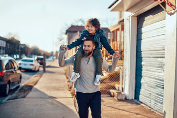 Father hugging his son while walking on a sidewalk in the suburbs of a city