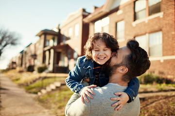 Father hugging his son while walking on a sidewalk in the suburbs of a city