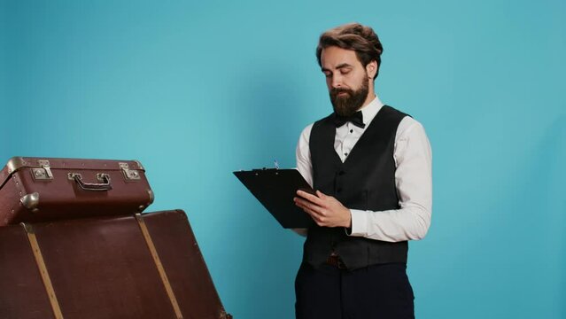 Doorman verifying checklist of guests, holding register log on clipboard to check hotel visitors in studio. Employee checking reservations on official ledger for archive, taking notes.