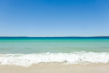 Fototapeta na wymiar Clear turquoise waters, cloudless blue skies, and sea foam on a sunny day at Callala Beach in Shoalhaven — Jervis Bay National Park, New South Wales, Australia