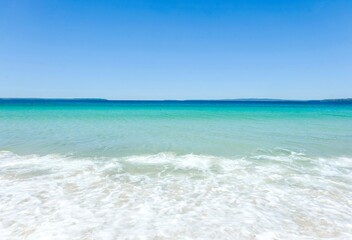 Fototapeta na wymiar Clear turquoise waters, cloudless blue skies, and sea foam on a sunny day at Callala Beach in Shoalhaven — Jervis Bay National Park, New South Wales, Australia