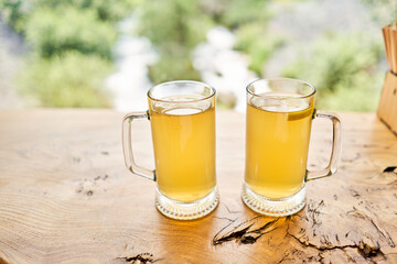 Two cups of ginger root tea with lemon, honey and mint on a wooden table and High-mountain river in the background. Walk in the mountains and relax in a cozy cafe. Hiking on a day off