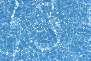 Blue water with ripples on the surface. Defocus blurred transparent blue colored clear calm water surface texture with splashes and bubbles. Water waves with shining pattern texture background.