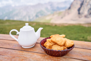Teapot with tea and delicious National Kazakh pastries baursak. Street cafe in the highlands with a view of the mountains.. Fry dough in boiling oil in a frying pan.