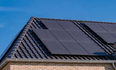 Black solar panels attached on the roof against a sunny sky Close up of new building with black...