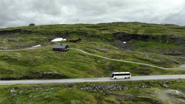 White tourist bus travelling past Norway mountain pass during summer - Sideways following aerial