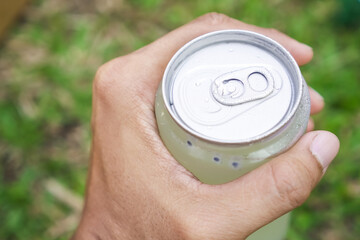 Someone hand holding Cold drinks in plastic transparent cans with bokeh grass lawn background. Concept for Healthy food, summer thirsty, hot temperature, global boiling, dehidration. Minuman Kaleng.