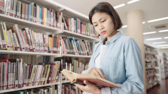 Asian female student studying in campus library Bookshelf Holding and Reading Text Book in library
