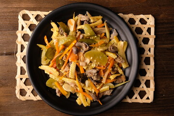 Sautéed baby corn, carrots, chicken gizzard liver, chilies, green tomatoes on a black plate on...