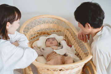 春の日中、自宅のゆりかごで眠る娘を優しい眼差しを向ける日本人の家族