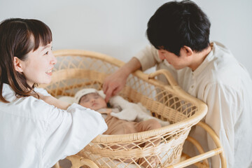 春の昼間、室内でゆりかごで眠る子どもを囲んで団欒する日本人の男女
