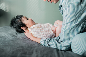 春の朝、ベッドで横たわる赤ちゃんの頭を支えて起こすアジア人の父親 - obrazy, fototapety, plakaty