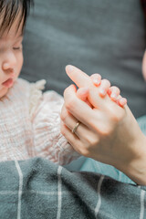 春の日中、ベッドで横たわって母親の手を握って眠る日本人の赤ちゃん