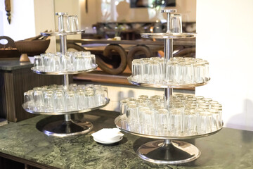 Many transparent drinking glass neatly arranged on racks. Kitchenware at hotel restaurant wedding buffet.
