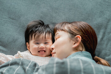 春の朝、ベッドで横たわって顔をくっつける日本人の母親と赤ちゃんの親子