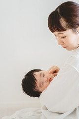 秋の朝、家で子どもを抱っこして指でその頬に触れる日本人の母親