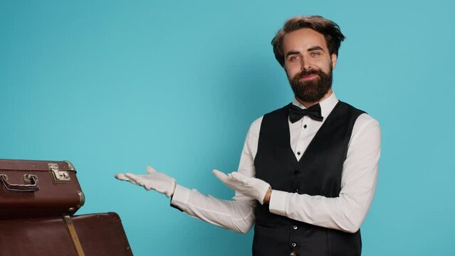 Doorkeeper shows left side in studio, wearing formal suit and tie while he does marketing ad to suggest direction sideways. Stylish classy hotel concierge worker presents advertisement.