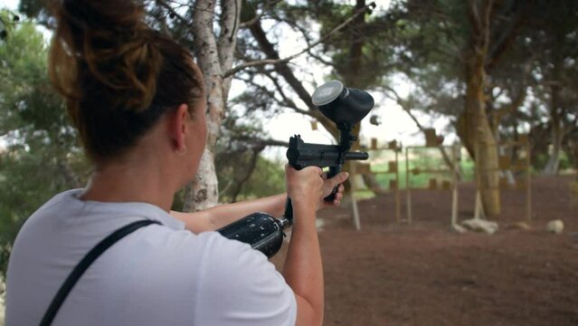 A woman shooing paintballs with a paint ball gun at a paintballing target range