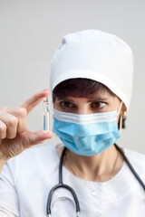 Woman doctor a mask holds an ampoule of a medical drug, close-up.