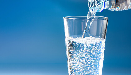 pouring water into a water glass, isolated drinking glass in front of a bright blue sunny and abstract background, close-up of a carbonated refreshing mineral water, beautiful concept with copy space - obrazy, fototapety, plakaty