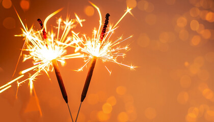two burning sparklers with shiny lights at the edge of modern abstract orange background, graphical...