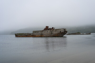 Old wooden shipwreck boat, foggy morning lonely shore. Abandoned antique old wooden ship at sea tropical landscape surrounded by fog. old ship. Selective focus.