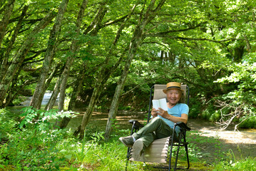 渓流のソロキャンプで読書を楽しむシニア男性