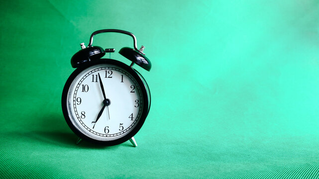 Background photo of an alarm clock showing 7:00 o'clock, isolated on green background