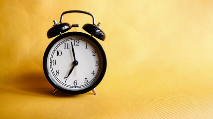 Background photo of an alarm clock showing 7:00 o'clock, isolated on yellow background