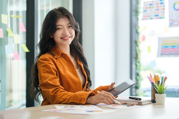 Smiling asian female graphic designer wearing  sitting front of computer sat her office.