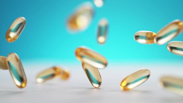 Yellow Fish Oil Softgel Capsules Falling on a White Clean Table and Bouncing on the Blue Background in Slow Motion